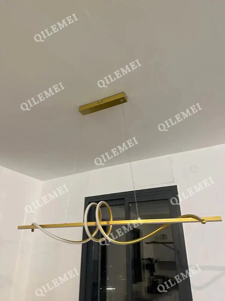 Modern gold pendant light hanging from ceiling, ideal for dining and living room decor. Minimalist design by QILEMEI.