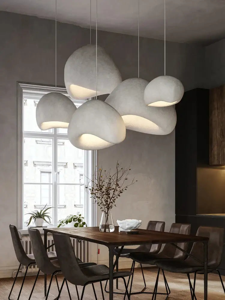 Modern pendant lights in a dining room above a wooden table with stylish chairs, enhancing minimalist home decor.