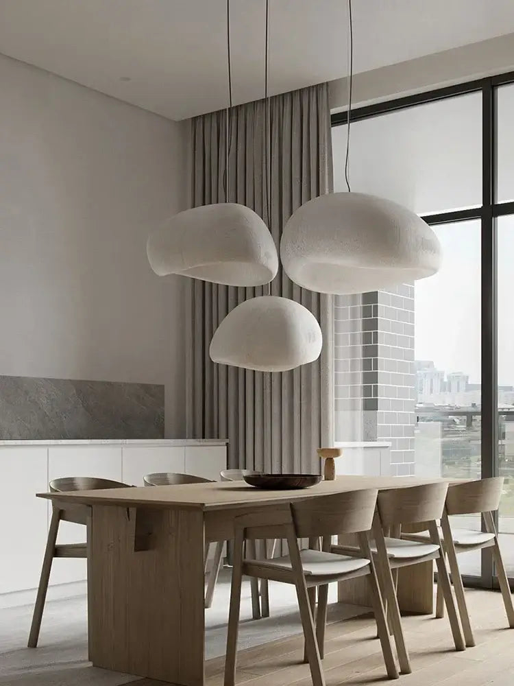 Modern pendant lights in a minimalist dining room, featuring two large cloud-shaped lamps over a wooden table.